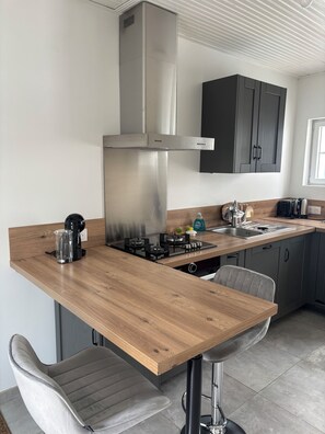 A modern kitchen with a wooden countertop, stainless steel range hood, and bar stools. - Two charming fishermen's cottages—just 500 meters from downtown and the beaches! (Saint-Gilles-Croix-de-Vie)