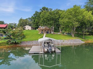 Une maison avec un quai s’avançant dans un lac paisible, entourée d’une végétation luxuriante et d’arbres.