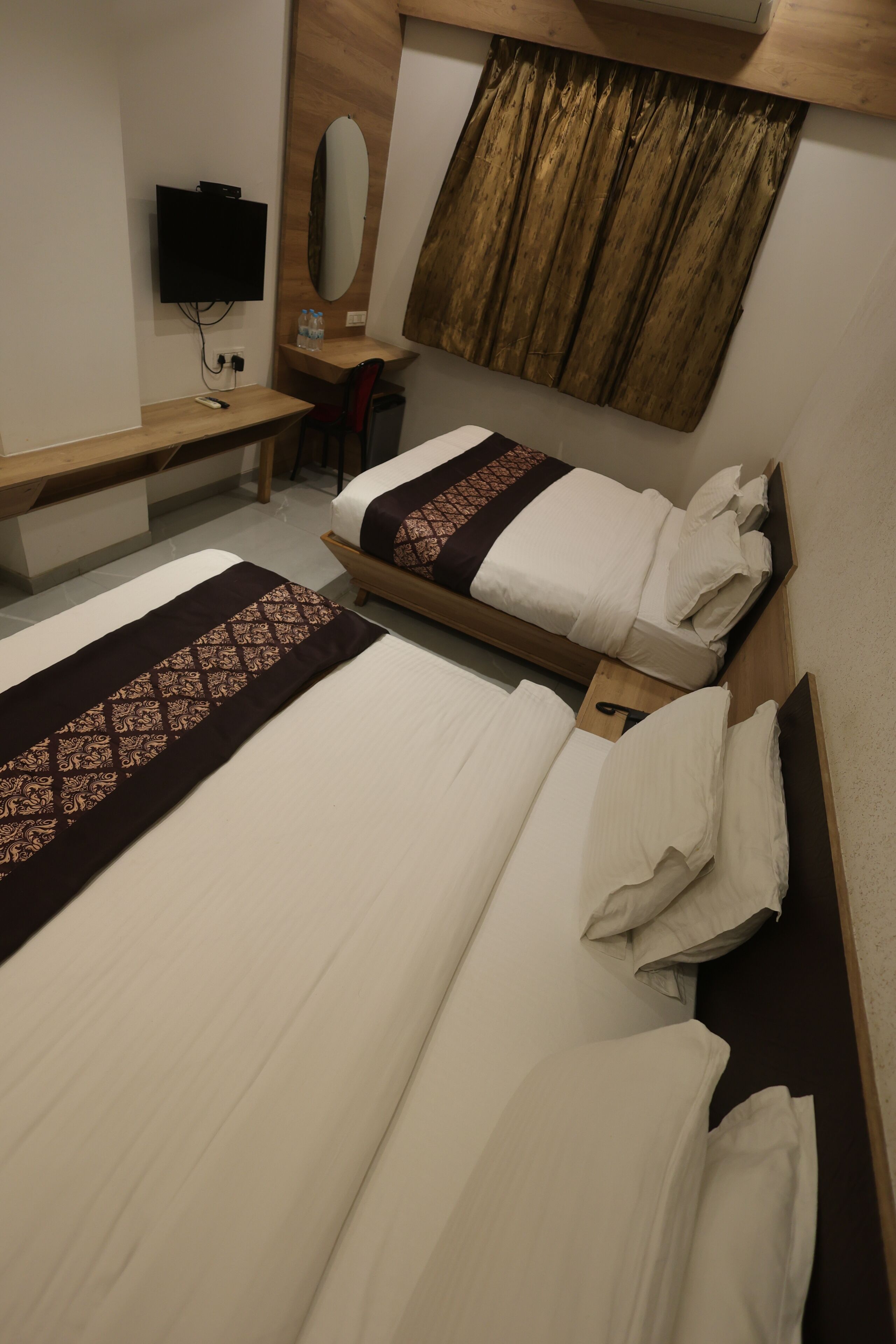Una habitación de hotel con dos camas, un escritorio, una silla, un televisor y un espejo.