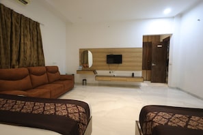 Una habitación de hotel moderna con sofá, cama, televisor y tocador de madera.