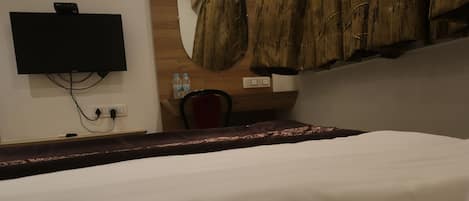 A hotel room with a bed, a flat-screen TV mounted on the wall, a wooden cabinet, and a round mirror.