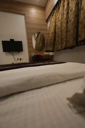 Une chambre d’hôtel comprenant un lit, un téléviseur à écran plat fixé au mur, une armoire en bois et un miroir rond.