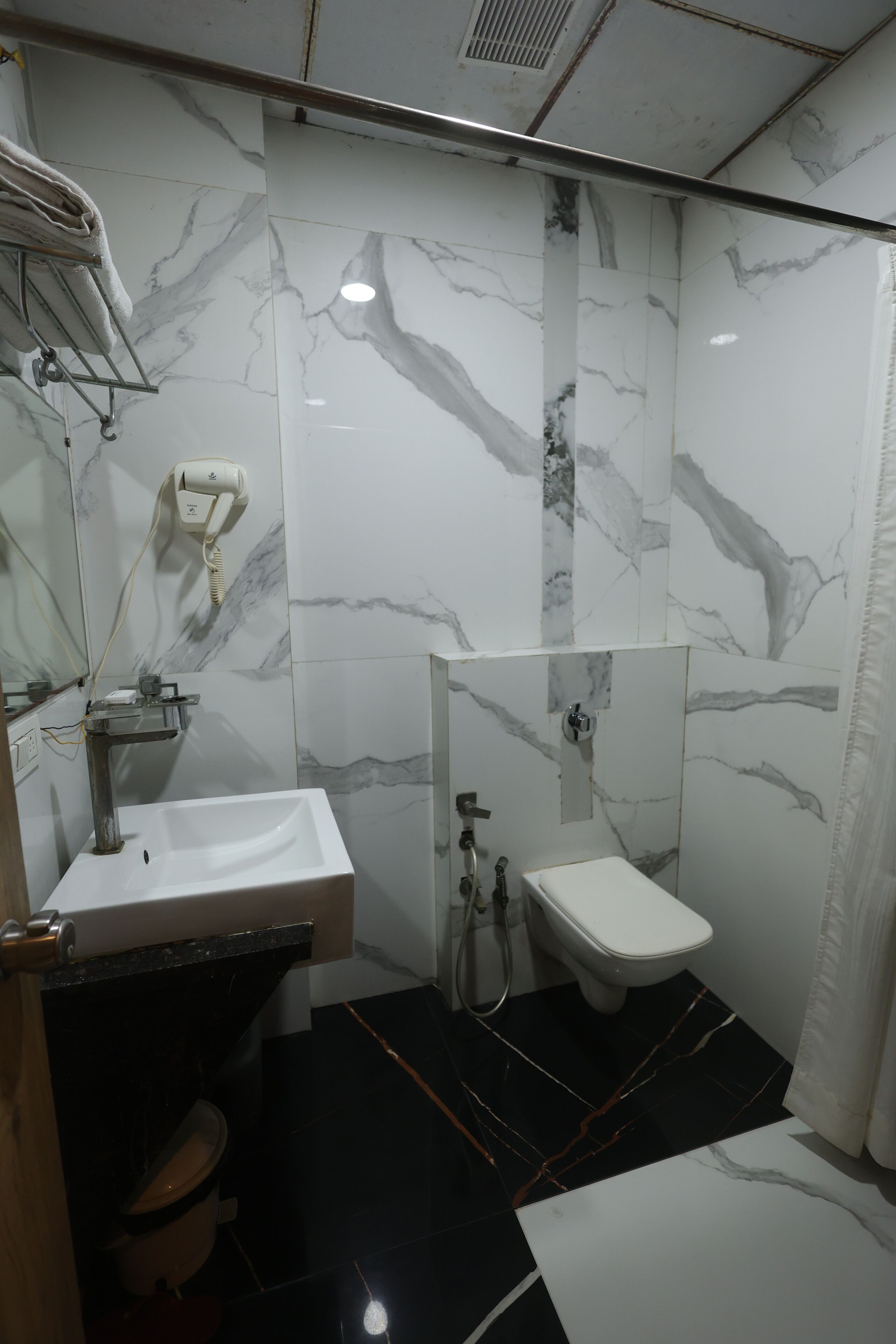 A bathroom with a sink, toilet, and shower area, featuring marble walls and black tiled flooring.