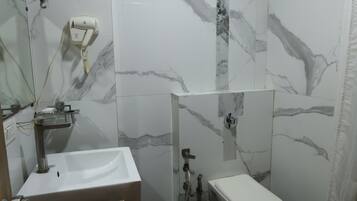A bathroom with a sink, toilet, and shower area, featuring marble walls and black tiled flooring.