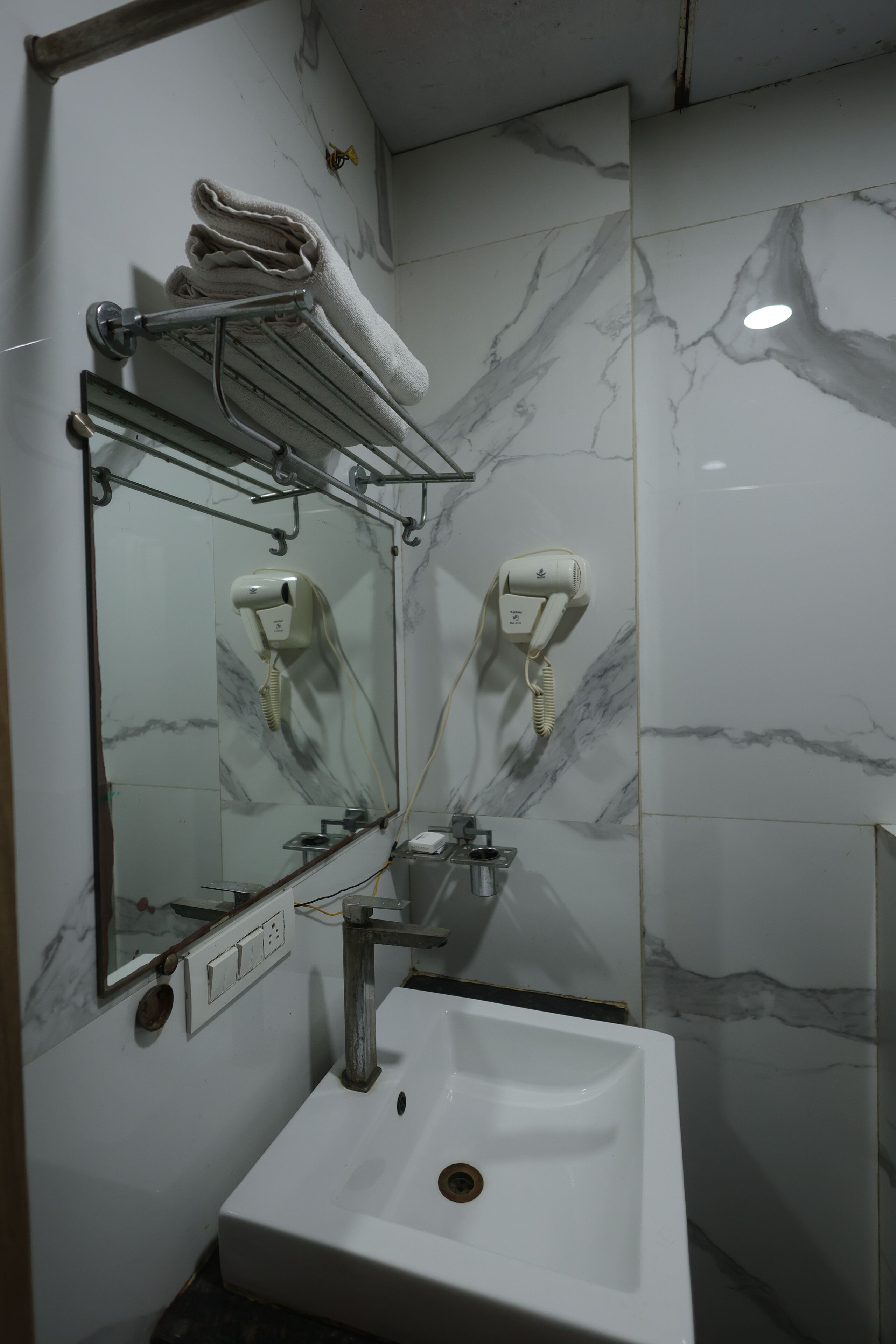 Un baño con lavamanos blanco, espejo, toallero y secador de pelo.