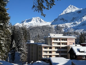 A multi-story building with a sign 'PARADISES' in the background, surrounded by snow-covered trees and mountains.