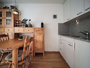 A modern kitchen with wooden cabinetry, a granite countertop, and a dining area with a wooden table and chairs.