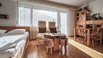 Ein Schlafzimmer mit einem hölzernen Bett, einem runden Holztisch und einem Stuhl. Es gibt eine Holzkommode mit Schubladen und eine Deckenleuchte.