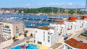 Uma marina com barcos, um edifício moderno com um jardim no terraço e vista para o porto.
