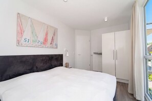 Quarto com cama grande, cabeceira, quadro na parede, abajur e guarda-roupa.