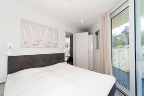 A hotel room with a large bed, a wall-mounted artwork, a door leading to a balcony, and a window with curtains. - Dünenvilla 10, Apartment 02 (Lübeck-Travemünde)