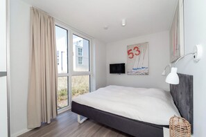 Ein Schlafzimmer mit einem Bett, einem Fernseher, einer Wandlampe und einem Fenster mit Vorhängen.