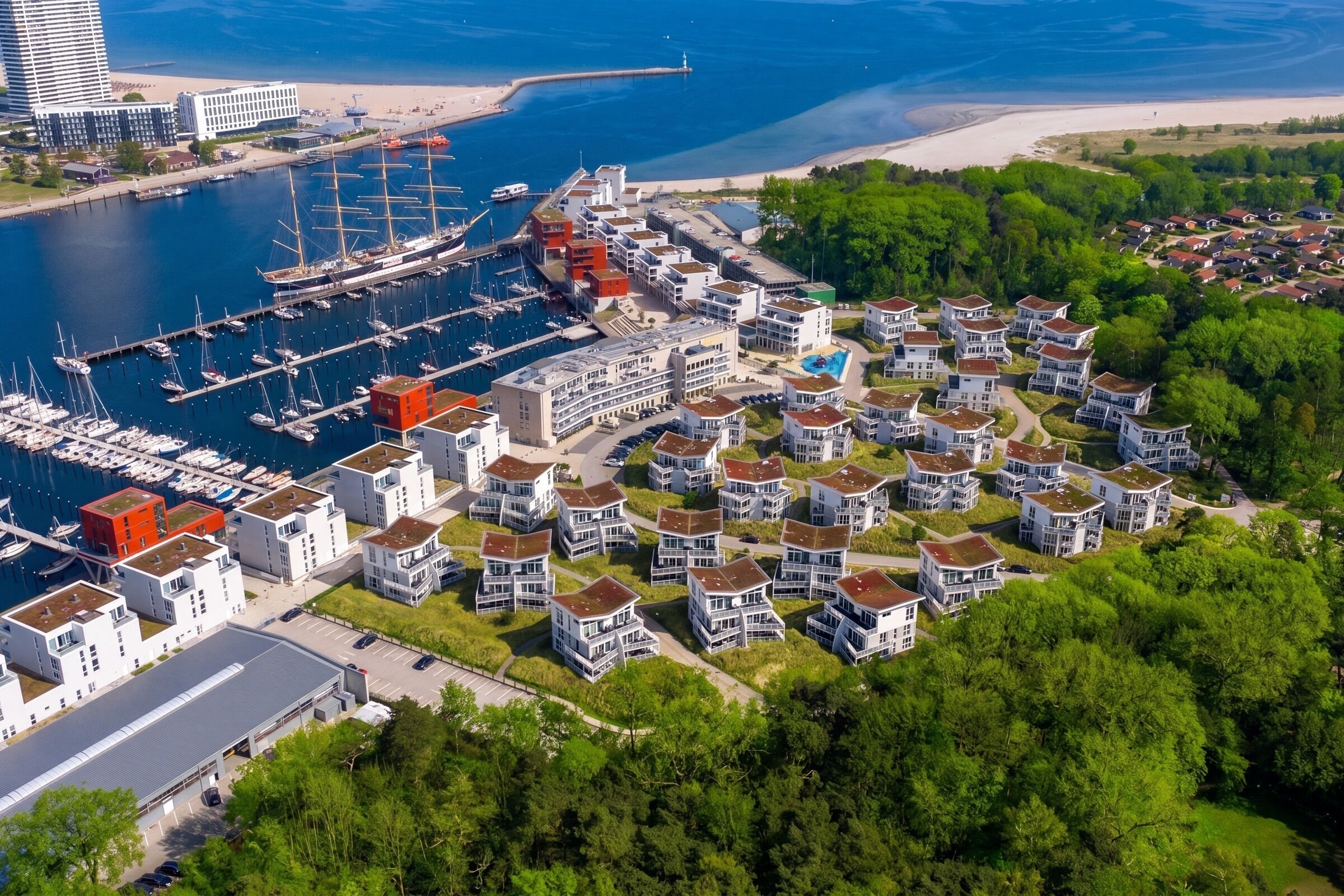 A coastal residential area with modern houses, a marina with boats, and a lighthouse in the distance.