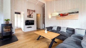 A modern living room with a sofa, a wooden coffee table, a TV, and a fireplace. - Fresh Breeze Vacation Home 23 (Lübeck-Travemünde)