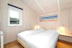 Ein Schlafzimmer mit einem Bett, einem Fenster, einem Bild und einem Nachttisch mit einer Lampe.