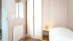 A bedroom with a wardrobe, a bedside table with a lamp, and a radiator. - Fresh Breeze Vacation Home 23 (Lübeck-Travemünde)