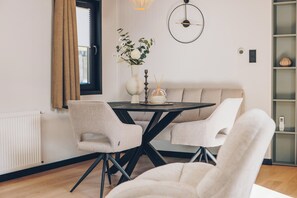Et moderne spiseområde med et rundt bord, to stole, en vase med blomster og et vægur.