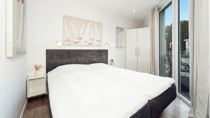 Quarto moderno com uma cama grande, cabeceira, mesa de cabeceira, espelho e janela com cortinas.
