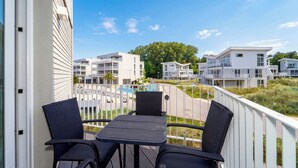 Varanda com duas cadeiras e uma mesa, com vista para uma piscina e edifícios vizinhos.