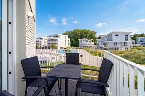A balcony with two chairs and a table, overlooking a swimming pool and adjacent buildings. - Dünenvilla 18, Apartment 05 (Lübeck-Travemünde)