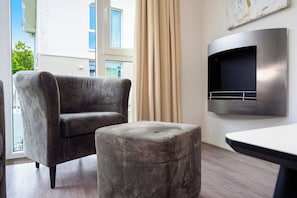 Ein modernes Wohnzimmer mit grauem Sofa, passendem Hocker und einem im Wand eingelassenen Fernseher.