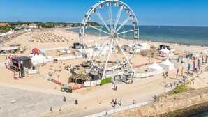 Uma praia com uma roda gigante, tendas e uma área arenosa com pessoas.