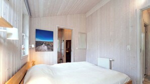Quarto com uma cama grande, paredes de madeira, um quadro e vista para um banheiro.