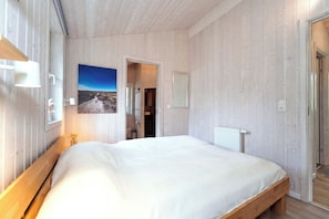 Ein Schlafzimmer mit einem großen Bett, Holzwänden, einem Gemälde und Blick auf ein Badezimmer.