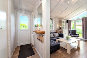 Ein modernes Wohnzimmer mit einer Couch, einem Couchtisch und einem Sessel. Eine Tür führt zu einem Balkon mit Blick ins Grüne.