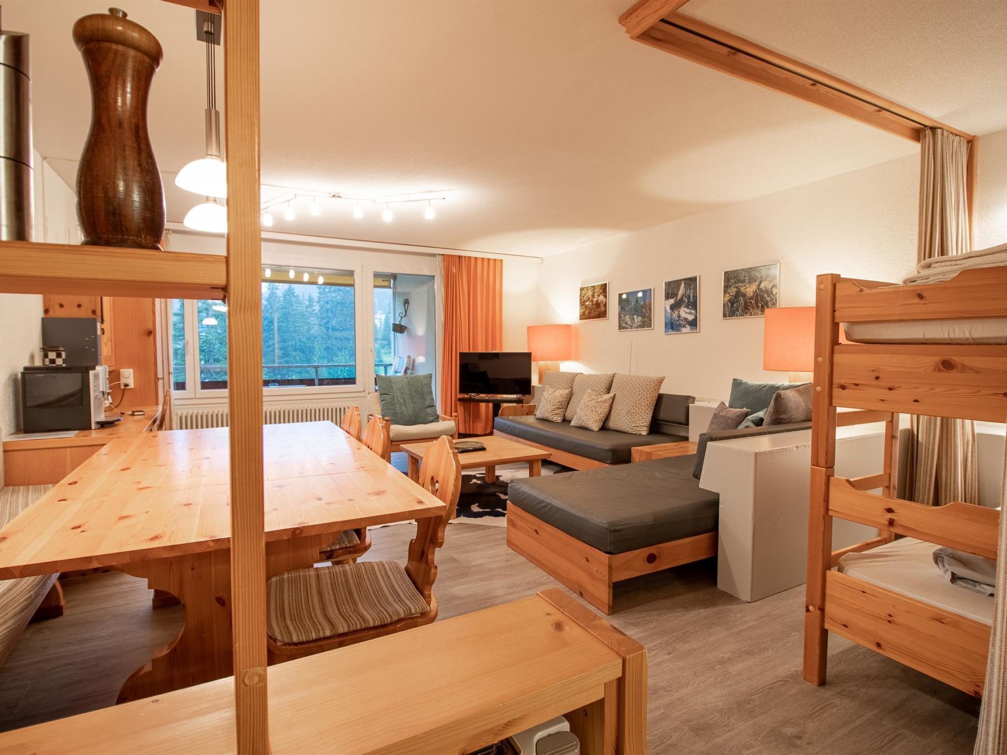 A cozy room with a wooden dining table, sofa, bunk beds, and a TV.