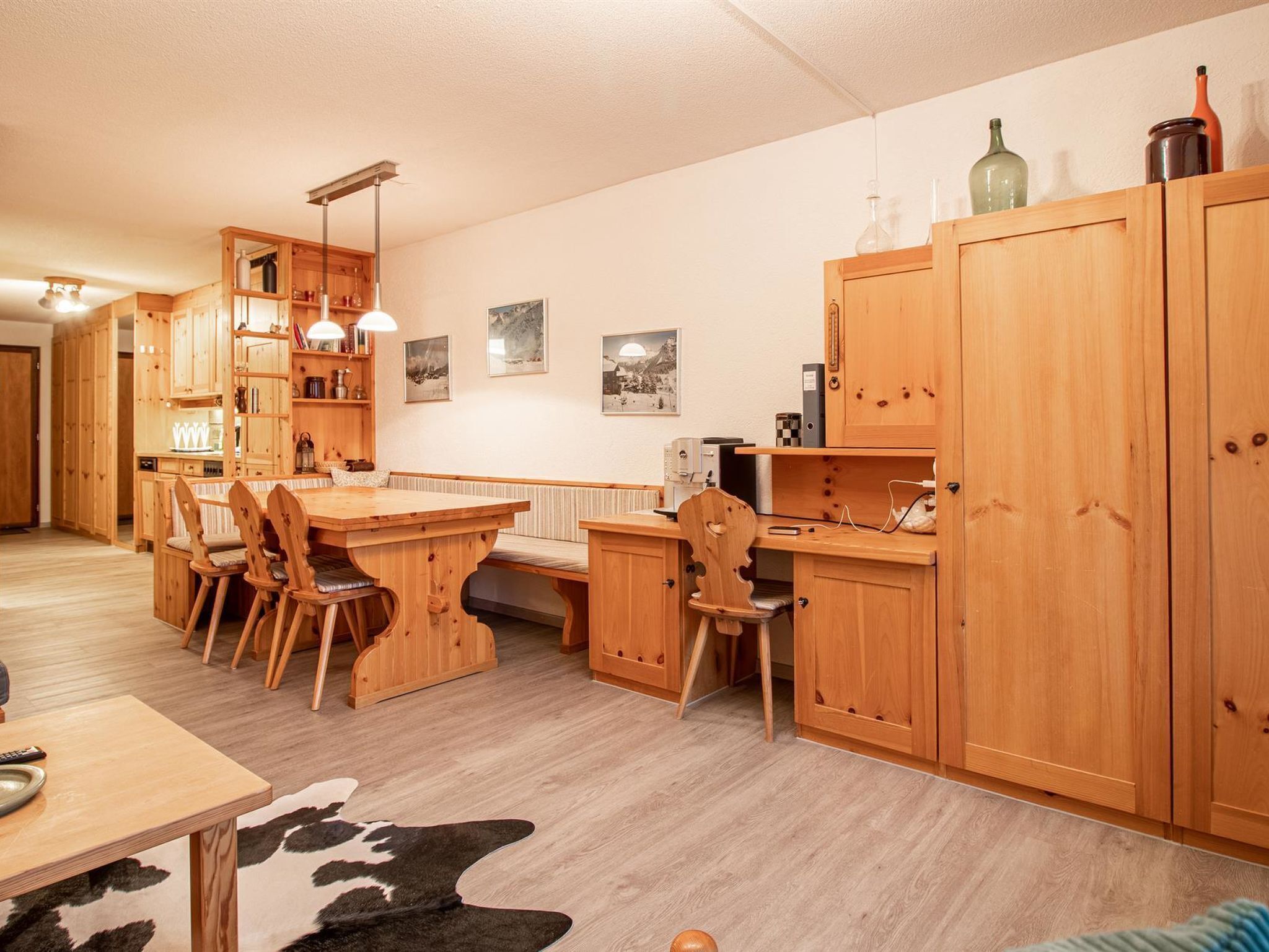 A wooden dining area with a table and chairs, a kitchen with wooden cabinets, and a living area with a sofa.