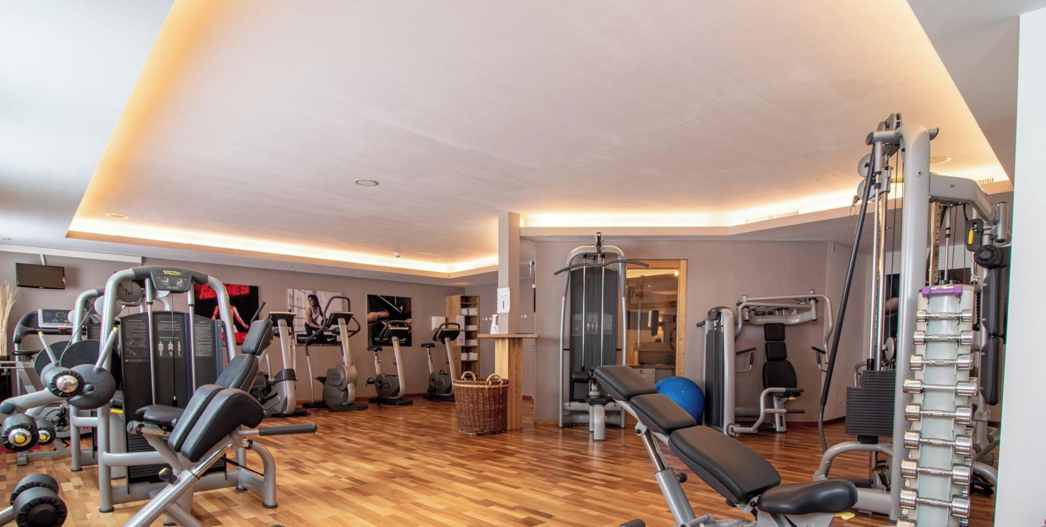 A gym with various exercise equipment, a wooden floor, and a wall-mounted TV.