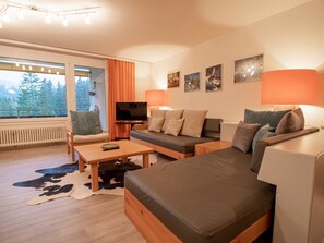 A modern living room with a sofa, a coffee table, and a TV. There are curtains, a lamp, and framed pictures on the wall. - Rothornblick 41 by Arosa Holiday Appartement/Fewo, Dusche oder Bad, WC, 6-Bettwo by Interhome (Arosa)