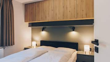 A hotel room with a bed, two bedside lamps, a wooden headboard, and a window with curtains.