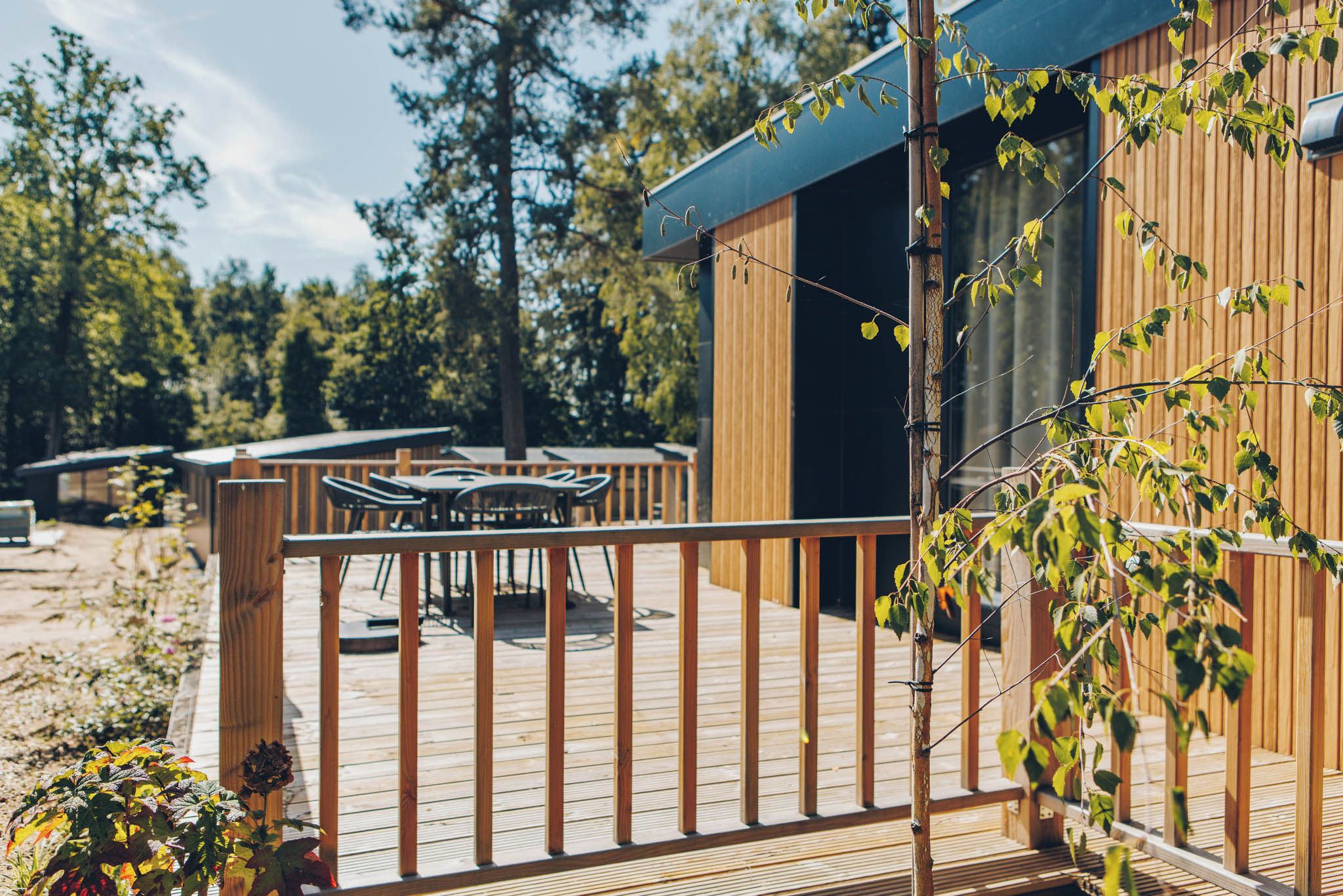Una terraza de madera con mesa y sillas, una valla de bambú y un edificio con techo oscuro.
