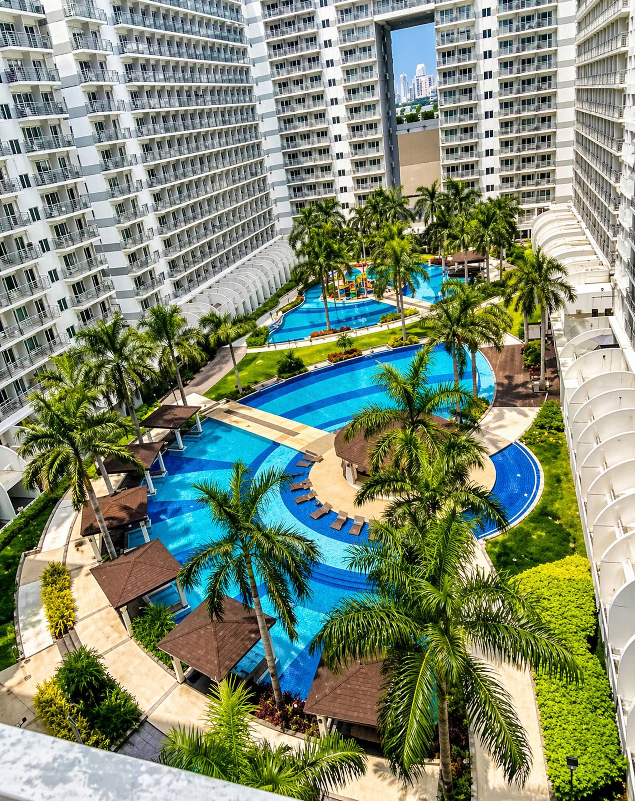 A multi-level hotel with a central swimming pool surrounded by palm trees and sun loungers.