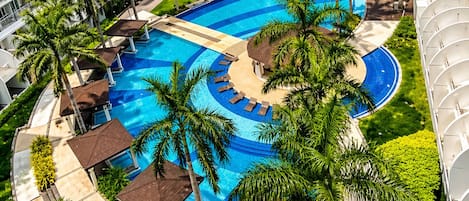 Un hotel de varios niveles con una piscina central rodeada de palmeras y tumbonas.