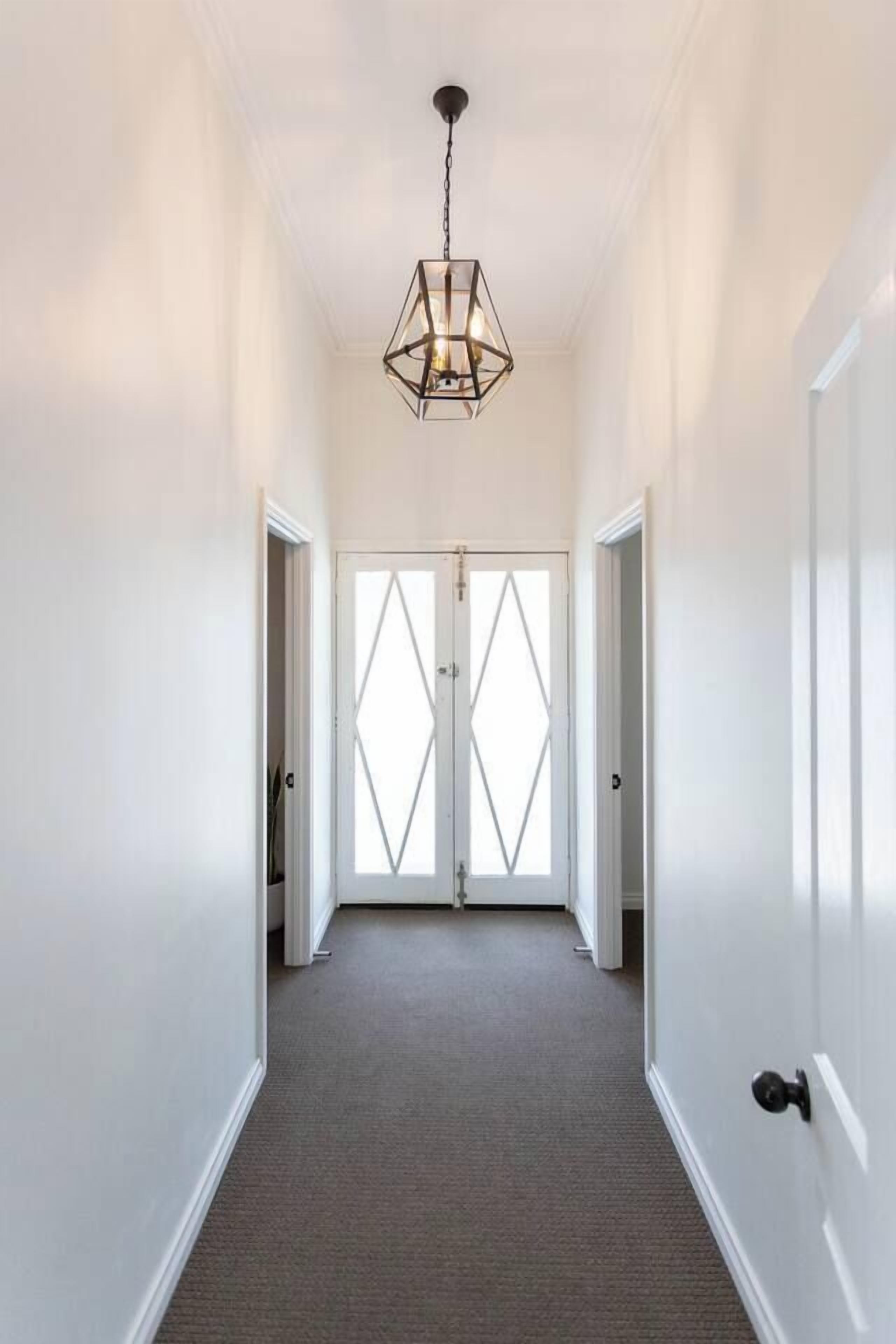 En gang med en dør med geometrisk mønster i enden, en hængende lampe og et tæppe på gulvet.