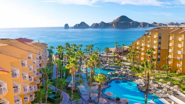 Een resort met een zwembad, palmbomen en uitzicht op zee.