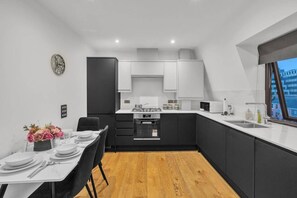 A modern kitchen with a dining area, featuring a stove, microwave, and sink. - 2-bed Apartment Near Canada Water (London)