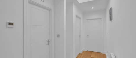 A hallway with white doors, a wooden floor, and a skylight.