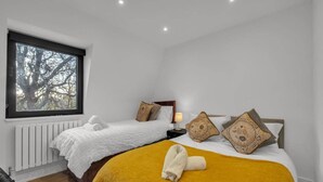 Een hotelkamer met twee bedden, een raam met uitzicht op bomen, een radiator en een lampje op het nachtkastje.