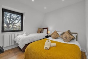 A hotel room with two beds, a window with a view of trees, a radiator, and a lamp on the nightstand. - 2-bed Apartment Near Canada Water (London)