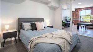 Een moderne slaapkamer met een bed, nachtkastjes en uitzicht op een eetruimte.