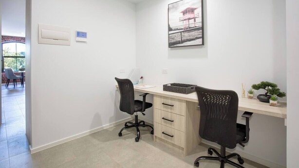 Een moderne kantoorruimte met twee zwarte bureaustoelen, een bureau met lades, een computer en een lijst aan de muur.