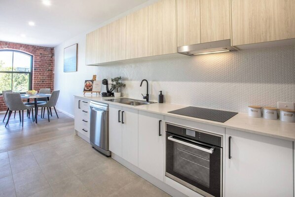 A modern kitchen with white cabinets, stainless steel appliances, and a large window.