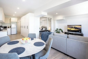 A modern living space with a dining area, a sofa, and a television. - Webb & Co Mid-Rise Apartment (Bendigo)