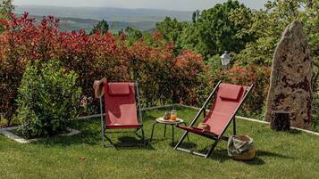 Dos sillones rojos con una mesita y una bebida, sobre un césped con vistas a un paisaje montañoso.