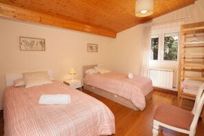 A bedroom with two beds, a wooden ceiling, a window with a view of trees, and a radiator.