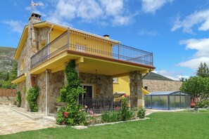 A two-story house with a balcony, stone exterior, and a garden with pink flowers.